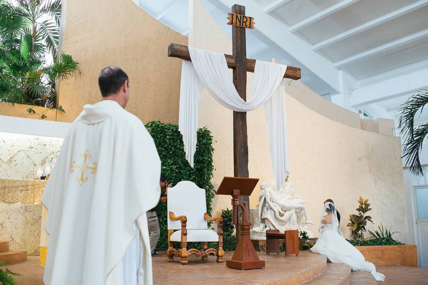 Catholic wedding ceremony at Cristo Resucitado Chapel Cancun with priest, altar cross and bride kneeling in prayer
