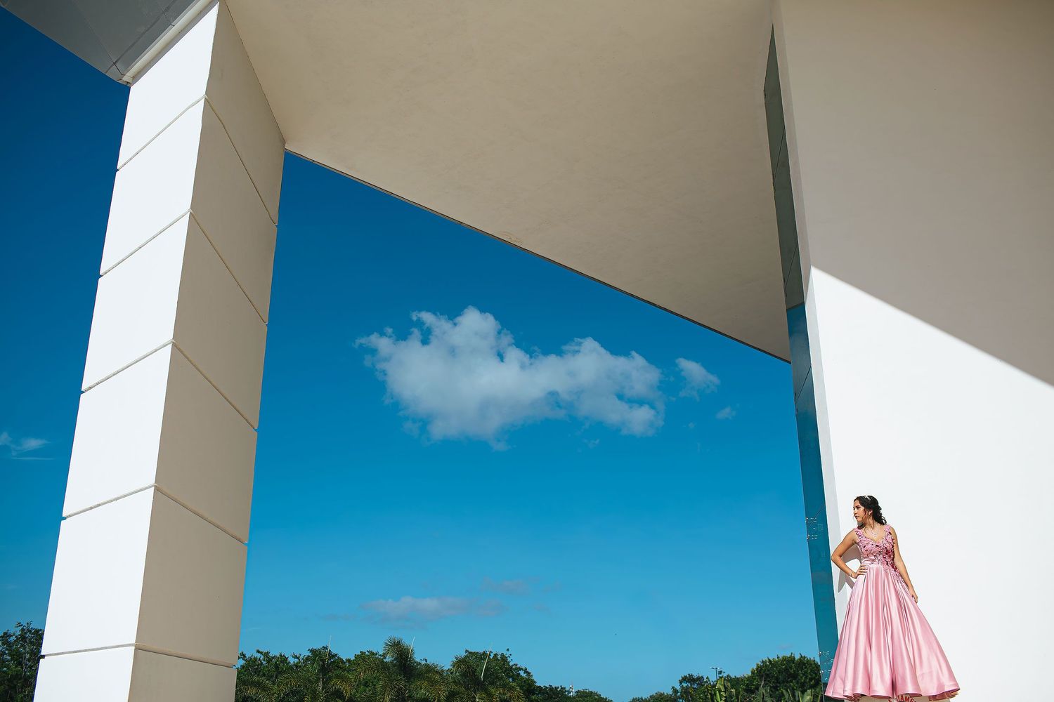 Quinceañera portrait session in Playa del Carmen featuring a young woman in a pink gown posing against modern architectural lines under a br