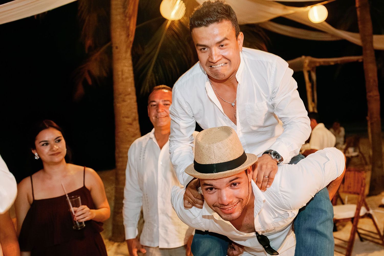 Two wedding guests share a playful piggyback moment during the late-night beach celebration.