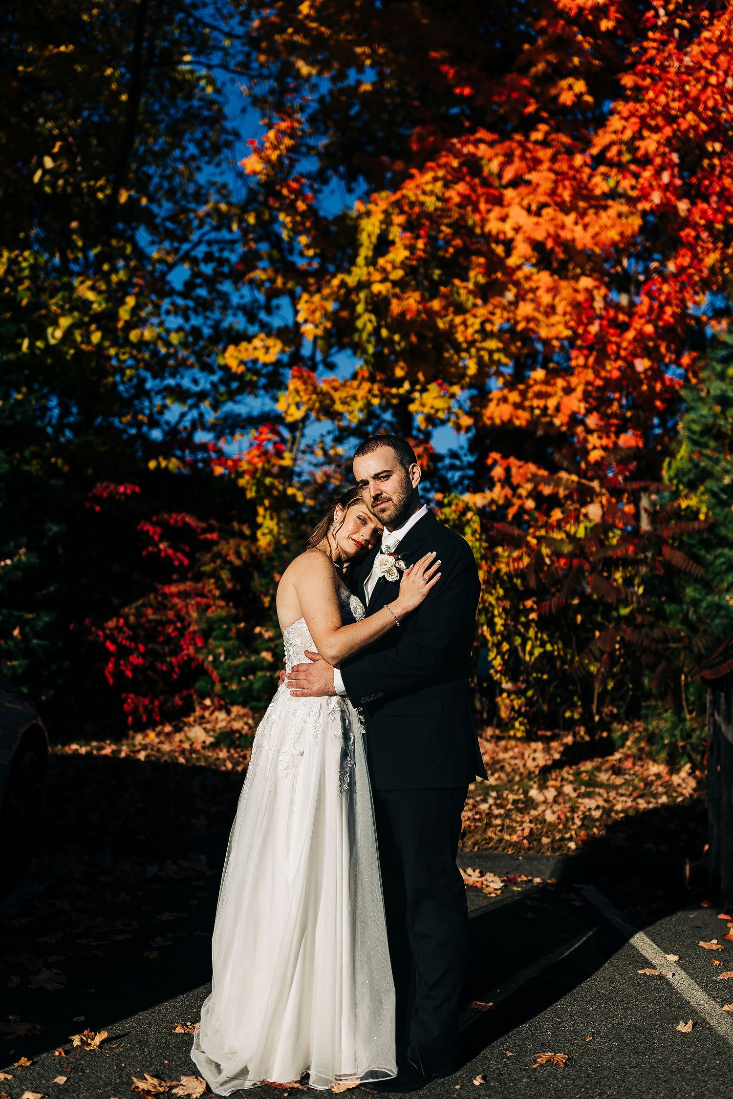 Brianna and Eddie embracing in their wedding attire beneath vibrant orange and red autumn leaves in Milwaukee.