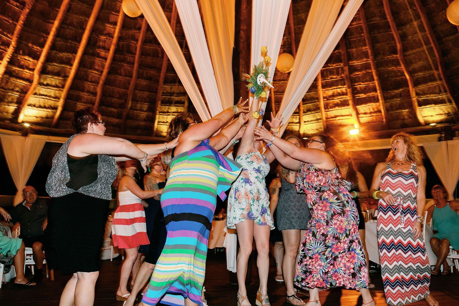 Guests reaching for the bouquet beneath the palapa’s thatched roof