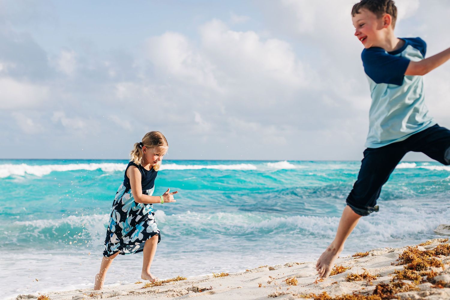 Children wearing coordinated blue beach outfits playing by the ocean during a family photo session in Cancun, Mexico.