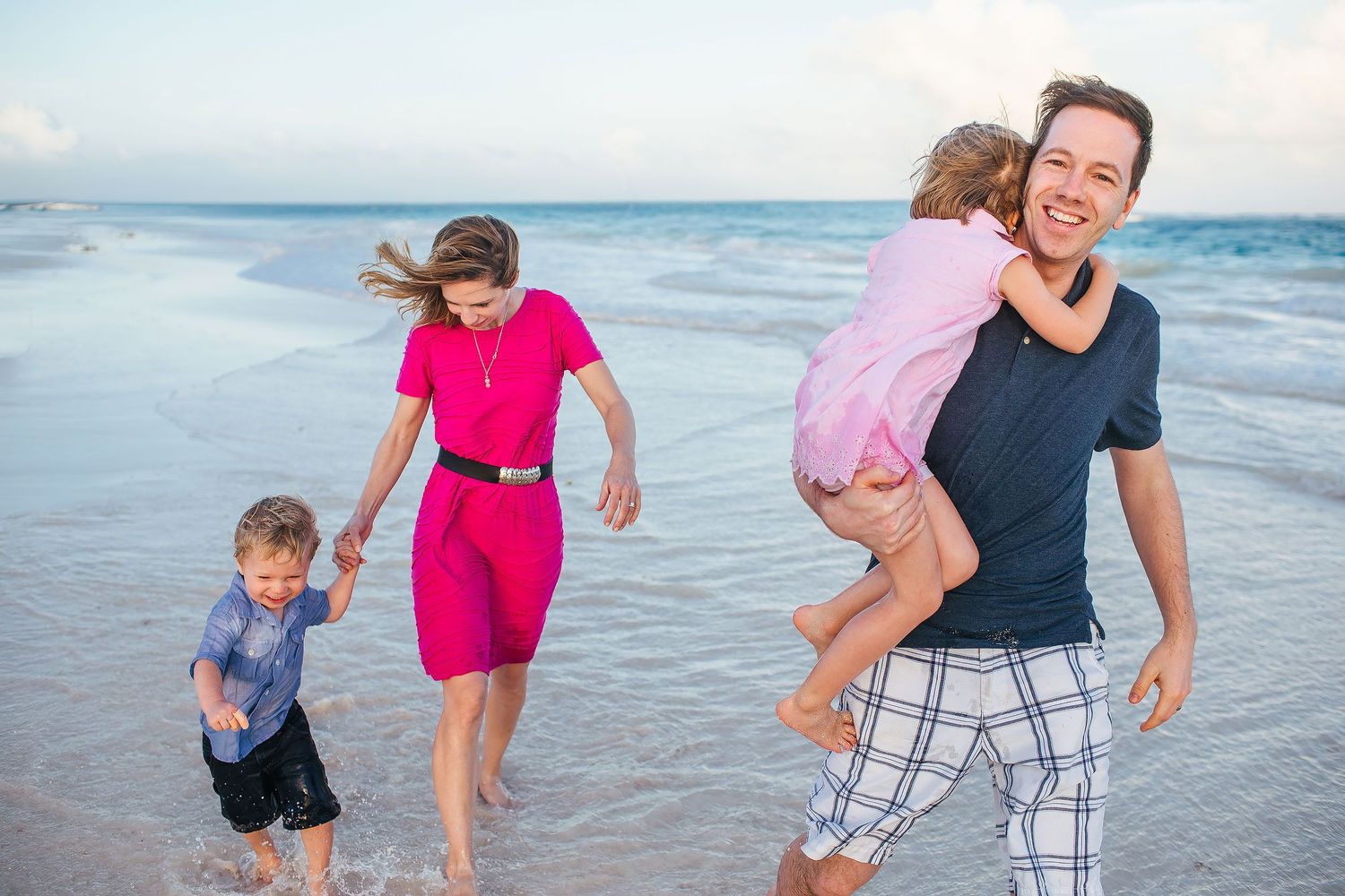 Family wearing colorful coordinated beach outfits during a playful sunset family photo session on the beach in Tulum, Mexico.