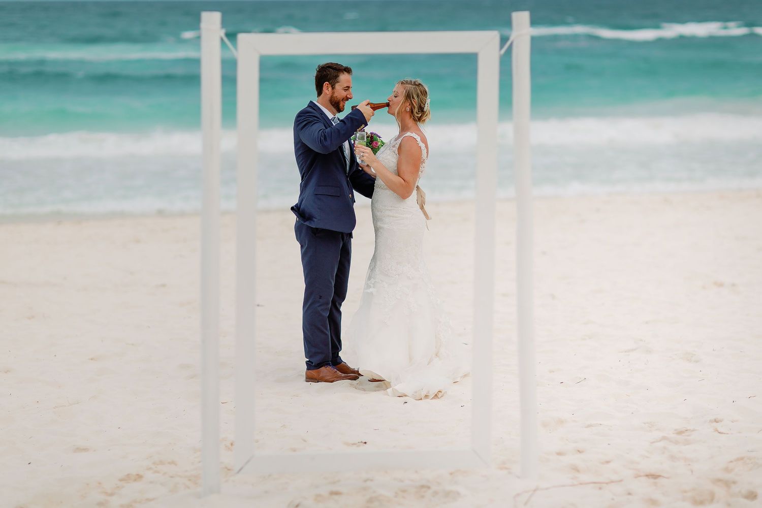 Matt offers Ashley a bottle during a playful newlywed moment framed against the Tulum beach.