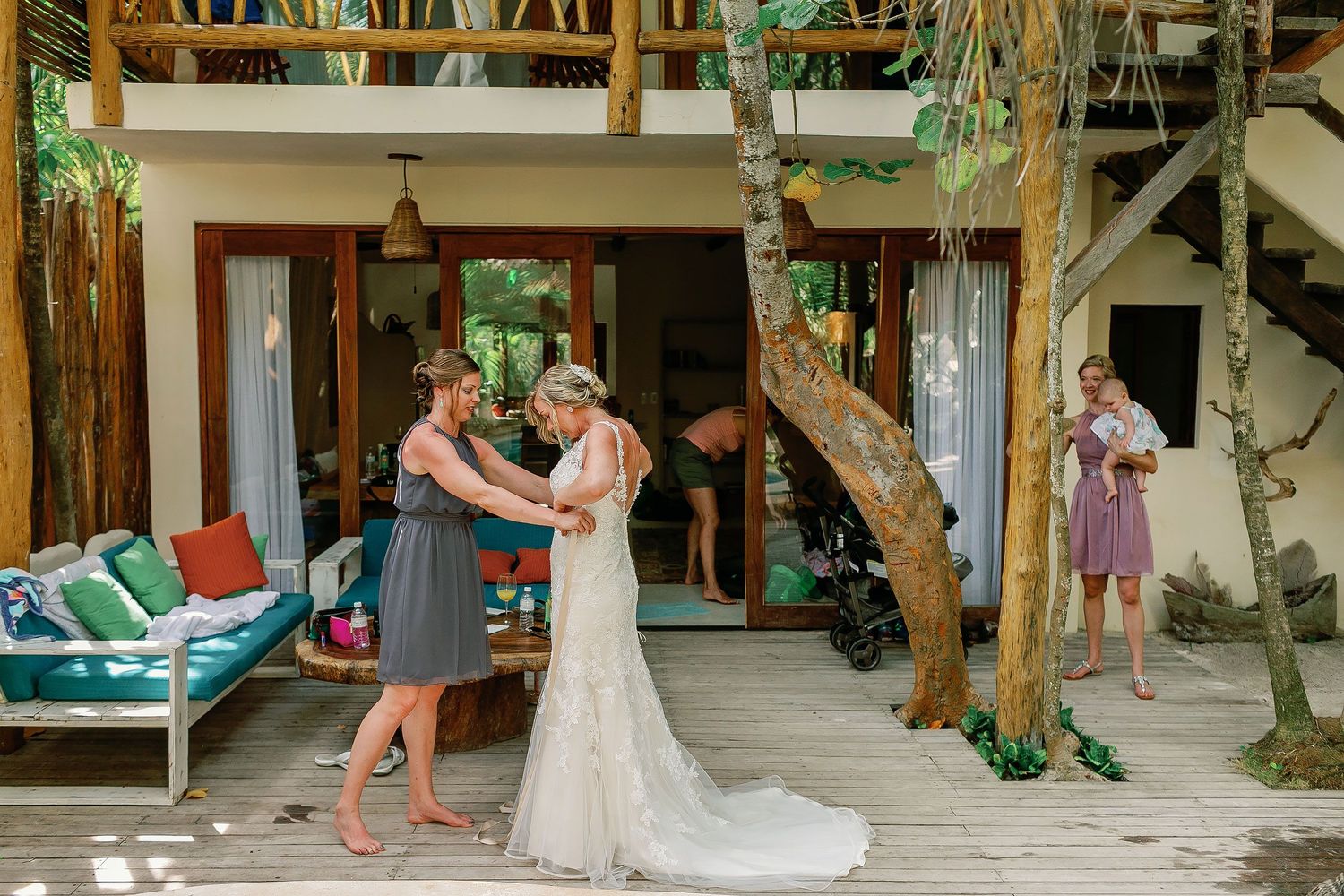 A friend helps Ashley fasten her lace wedding dress on the wooden deck of a private Tulum house.