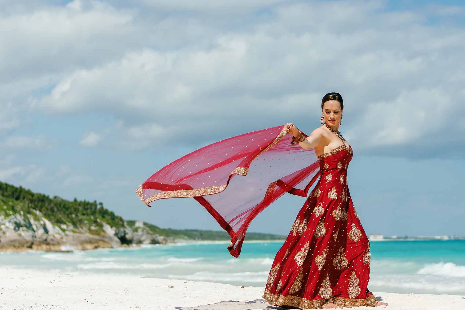 Elegant Indian bride portrait on Tulum beach with flowing red dupatta and turquoise Caribbean ocean during luxury Hindu destination wedding