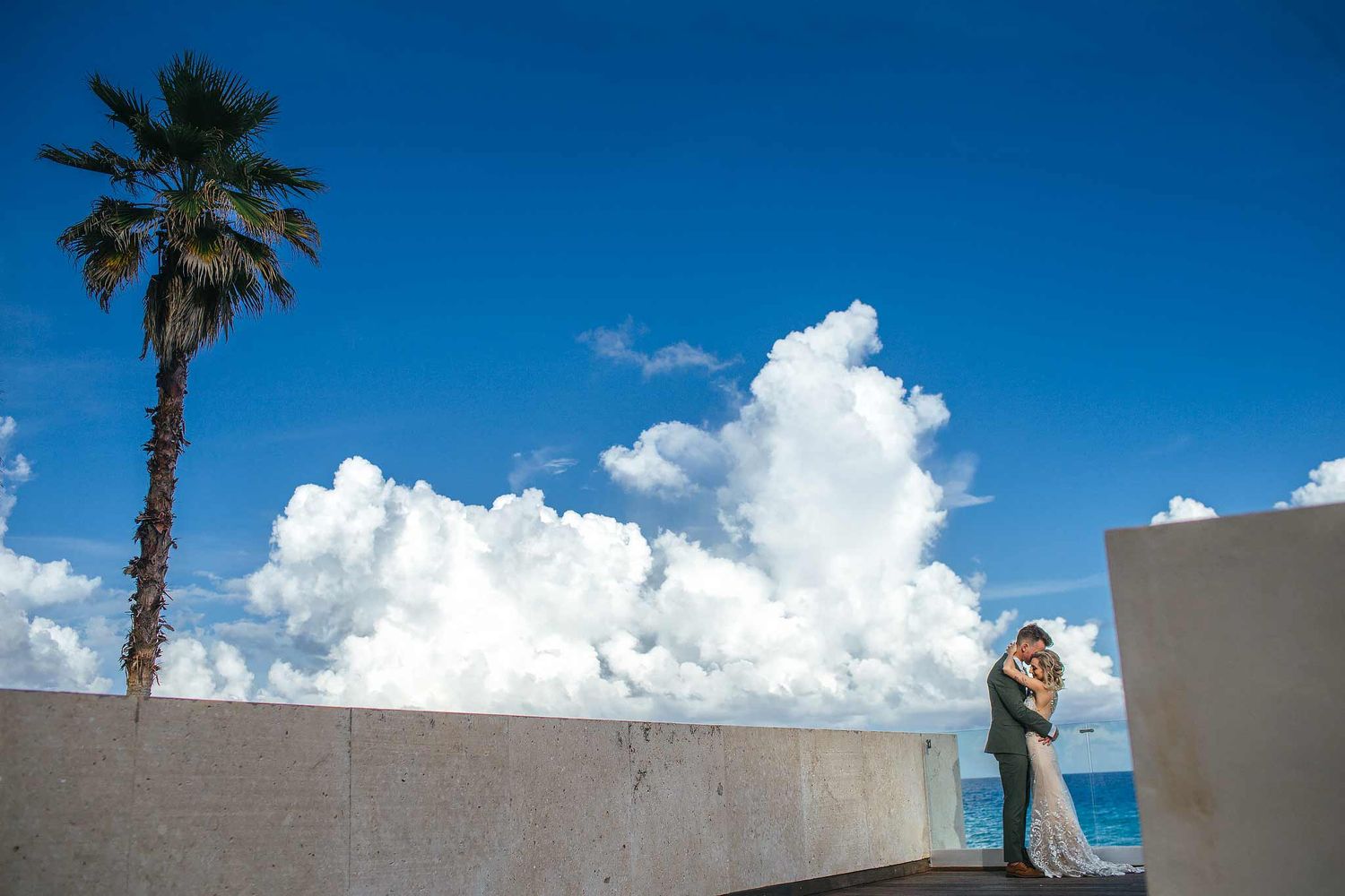 Romantic destination wedding photography in Cancun featuring a bride and groom embracing by the ocean with dramatic sky and tropical scenery