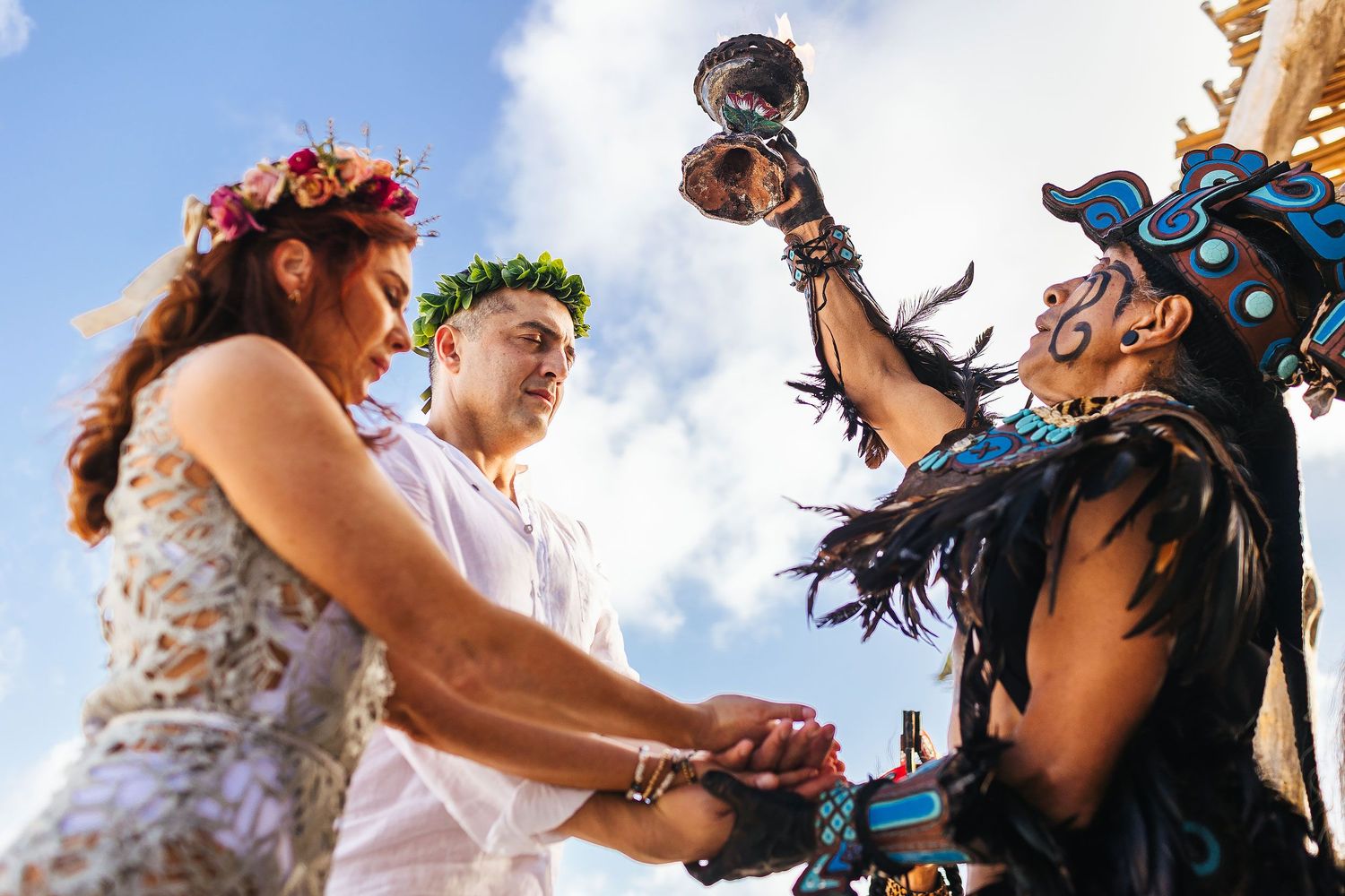 Sarah and Evish hold hands as a ceremonial leader raises a smoking vessel.