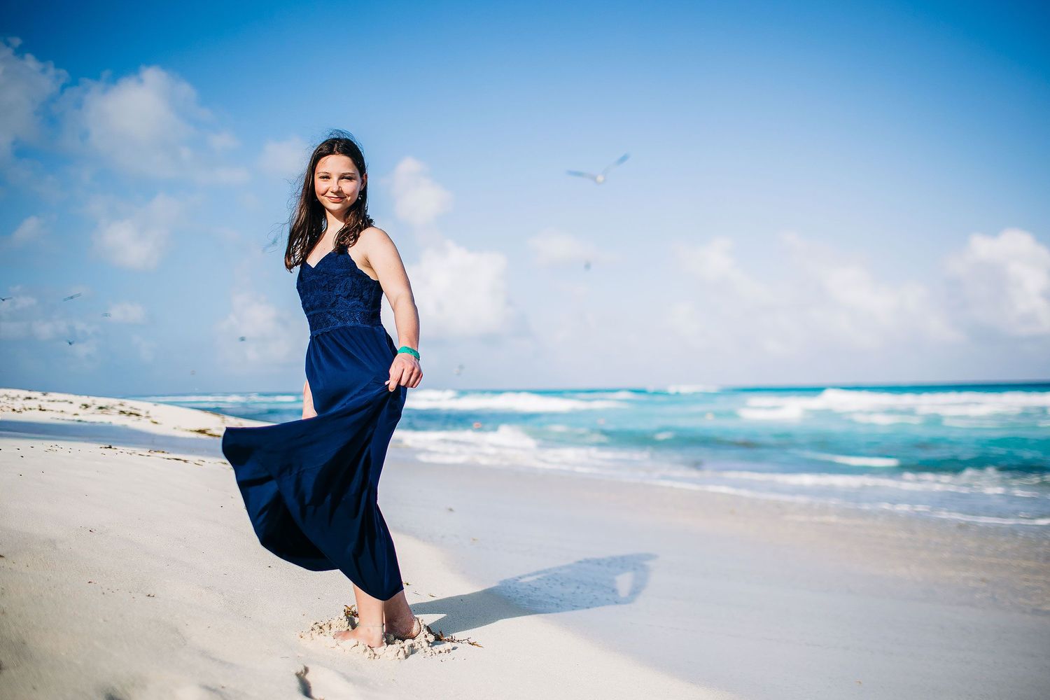 Senior portraits in Cancun with a flowing blue dress, ocean waves, bright skies, and the Caribbean coastline backdrop.