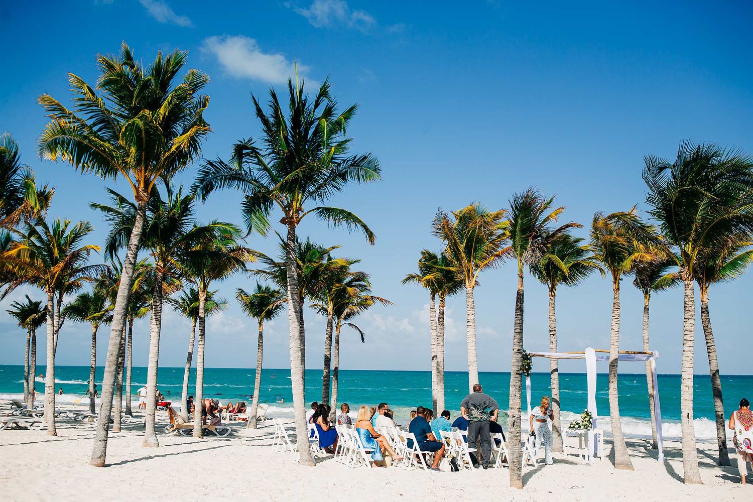Beach wedding setup at Riu Costa Mujeres with palm trees, white sand, turquoise Caribbean water, and oceanfront ceremony arch.