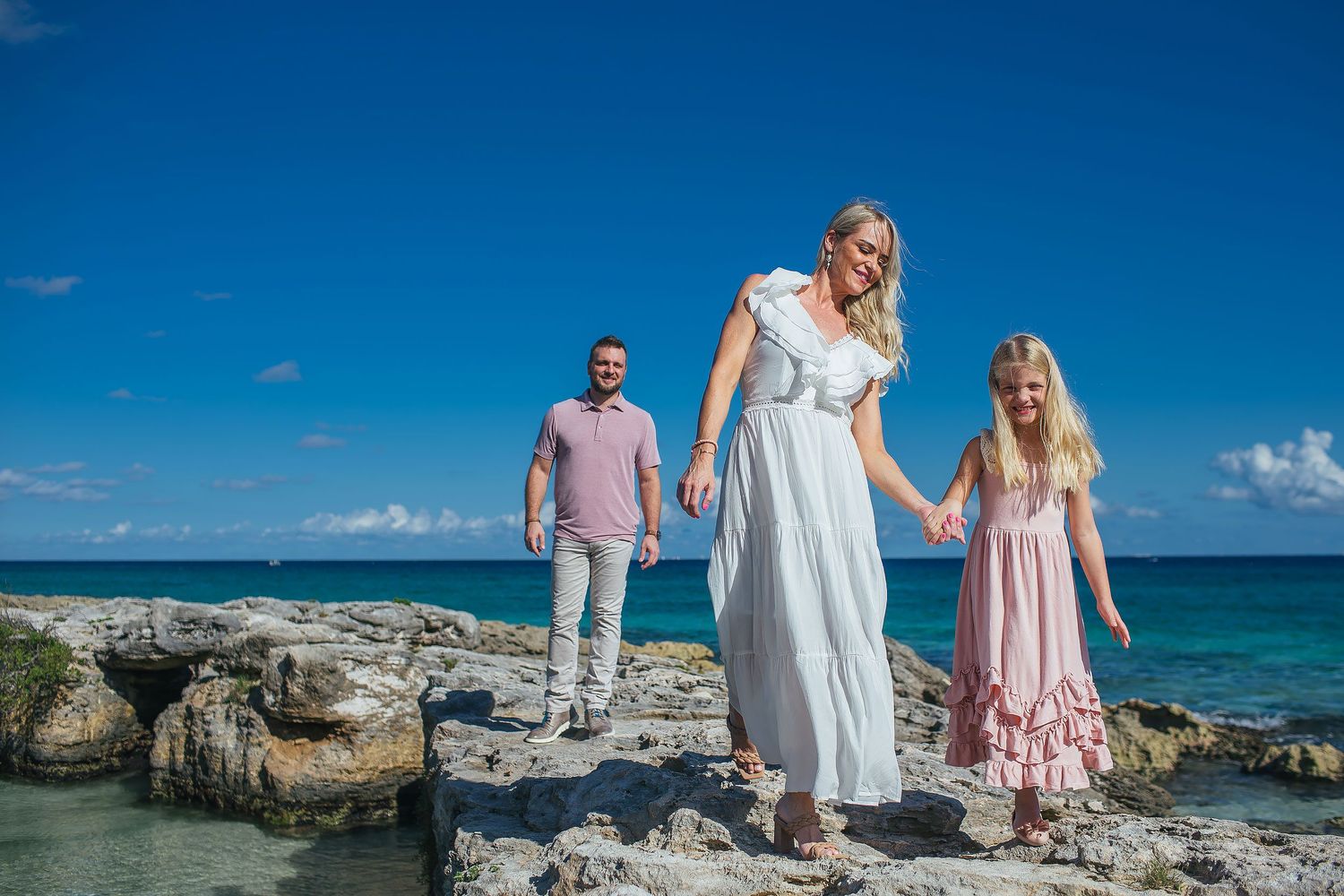 Family dressed in soft neutral beach outfits during a Riviera Maya family photo session by the ocean in Playa del Carmen.