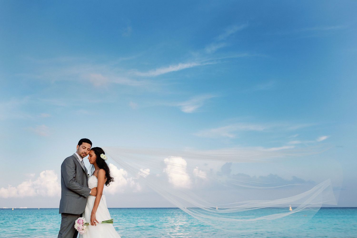 Felicitas and Keith pose beside the Caribbean as her long veil flows in the breeze.