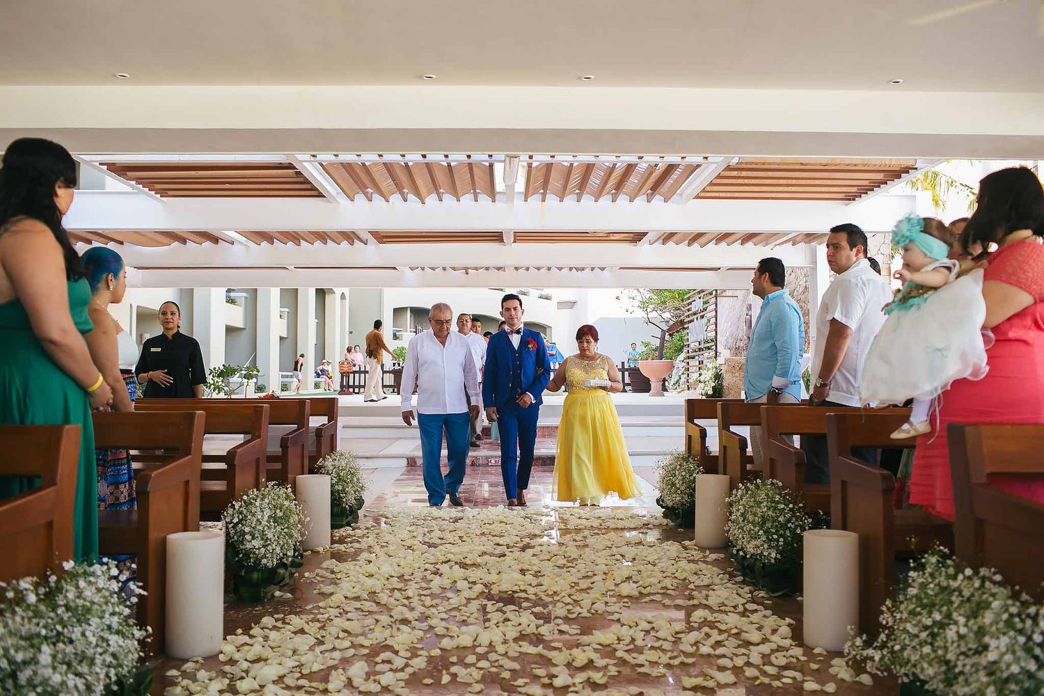 Groom walking down aisle at Sunscape Cancun Catholic wedding chapel with floral decorations and guests during ceremony