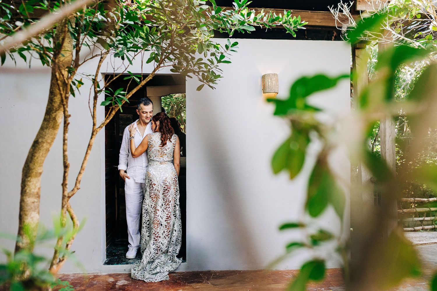 Sarah and Evish share a quiet moment in a white doorway surrounded by tropical greenery.