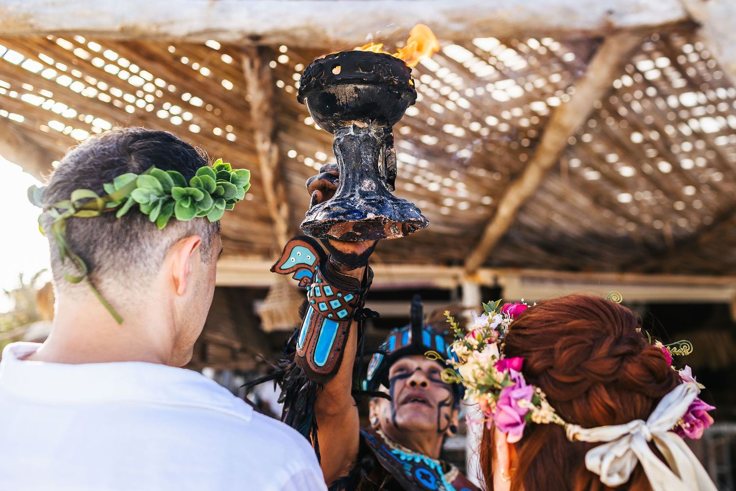 A ceremonial participant holds a flaming vessel above Sarah and Evish.