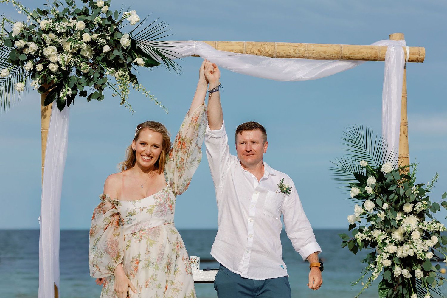 Autumn and Brian celebrating as newlyweds beneath their floral wedding arch at Dreams Sapphire.