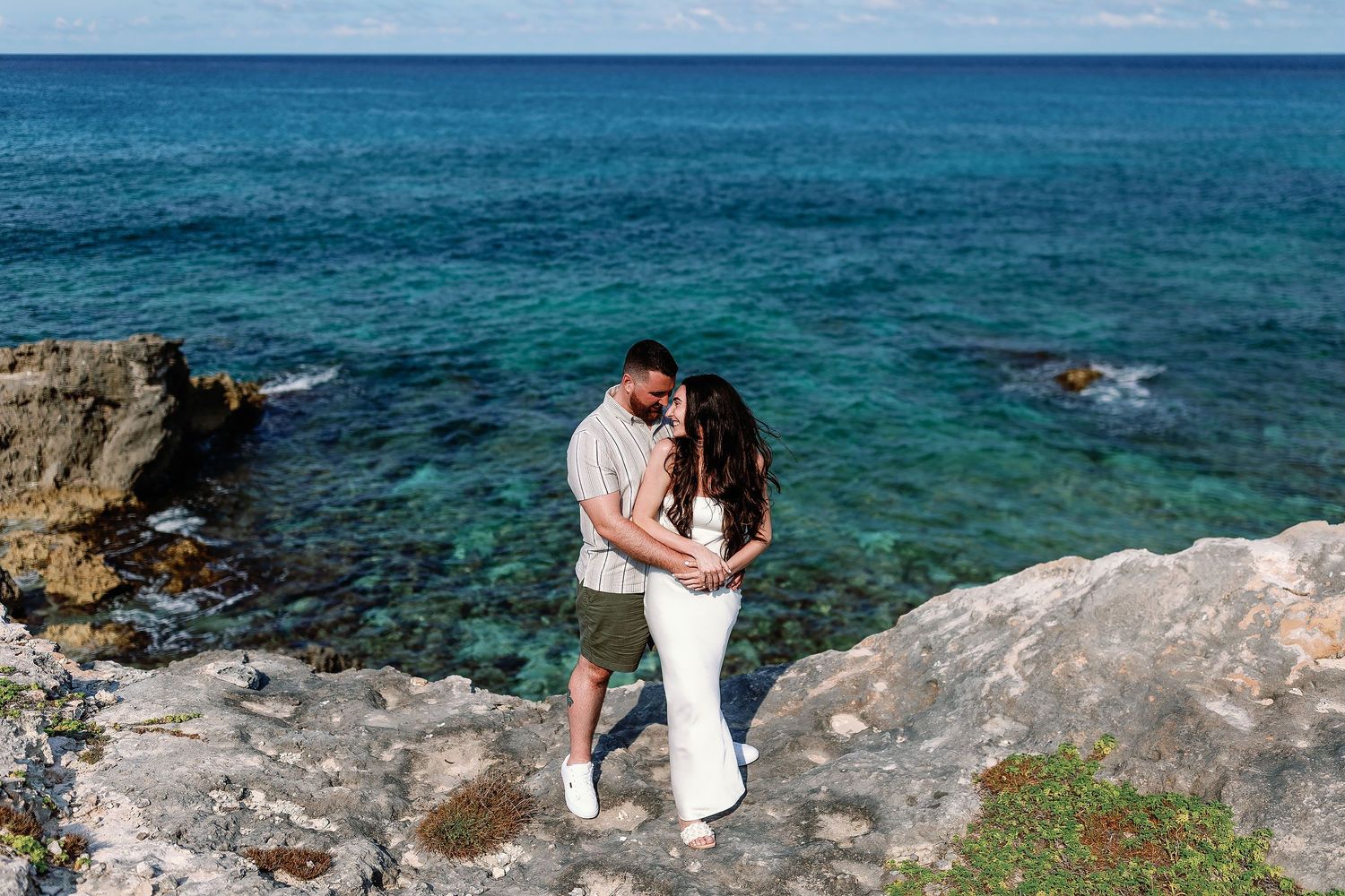 Alexia and Sam embrace on a rocky overlook above the turquoise Caribbean Sea at Punta Sur.