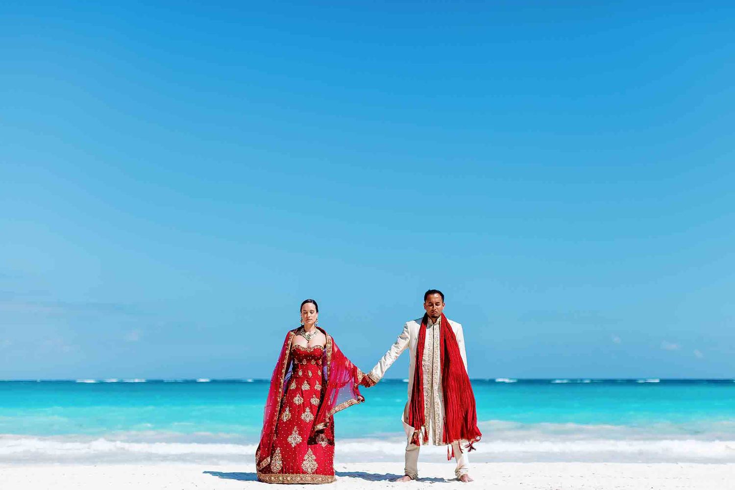 Indian wedding couple holding hands on white sand beach in Cancun Riviera Maya with turquoise Caribbean ocean during luxury destination wedd