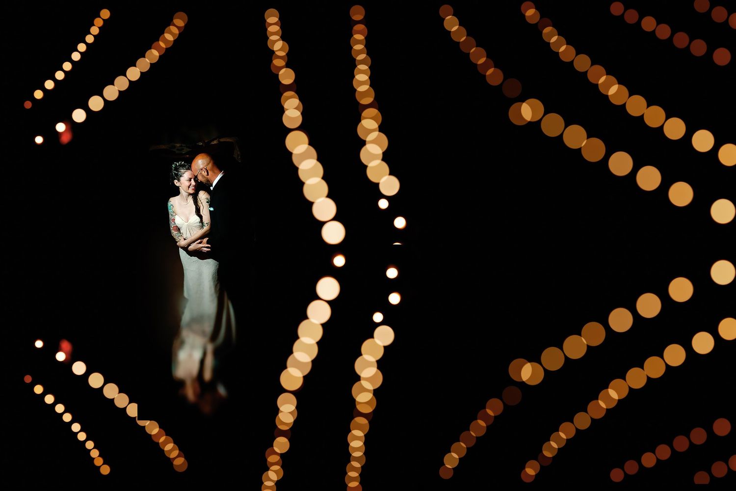 Elsie and Vincent sharing a close moment in their wedding attire, framed by softly blurred golden string lights in Minneapolis.