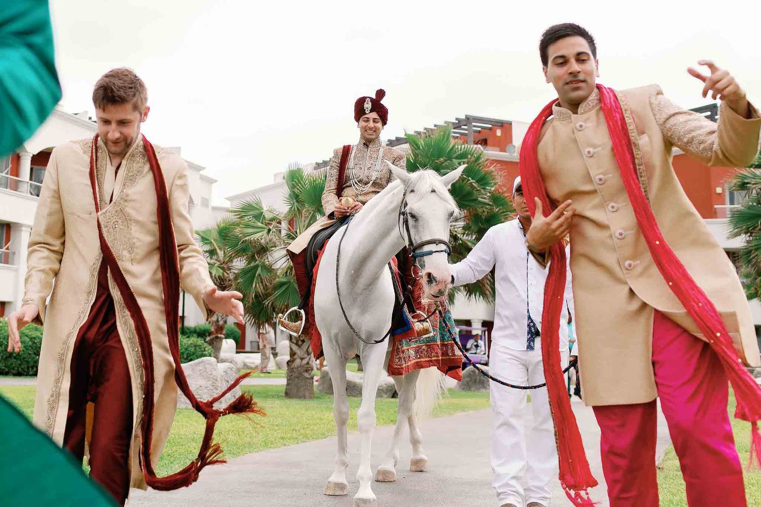 Indian groom arriving on white horse during vibrant baraat procession at luxury Riviera Maya destination wedding with guests dancing in trad
