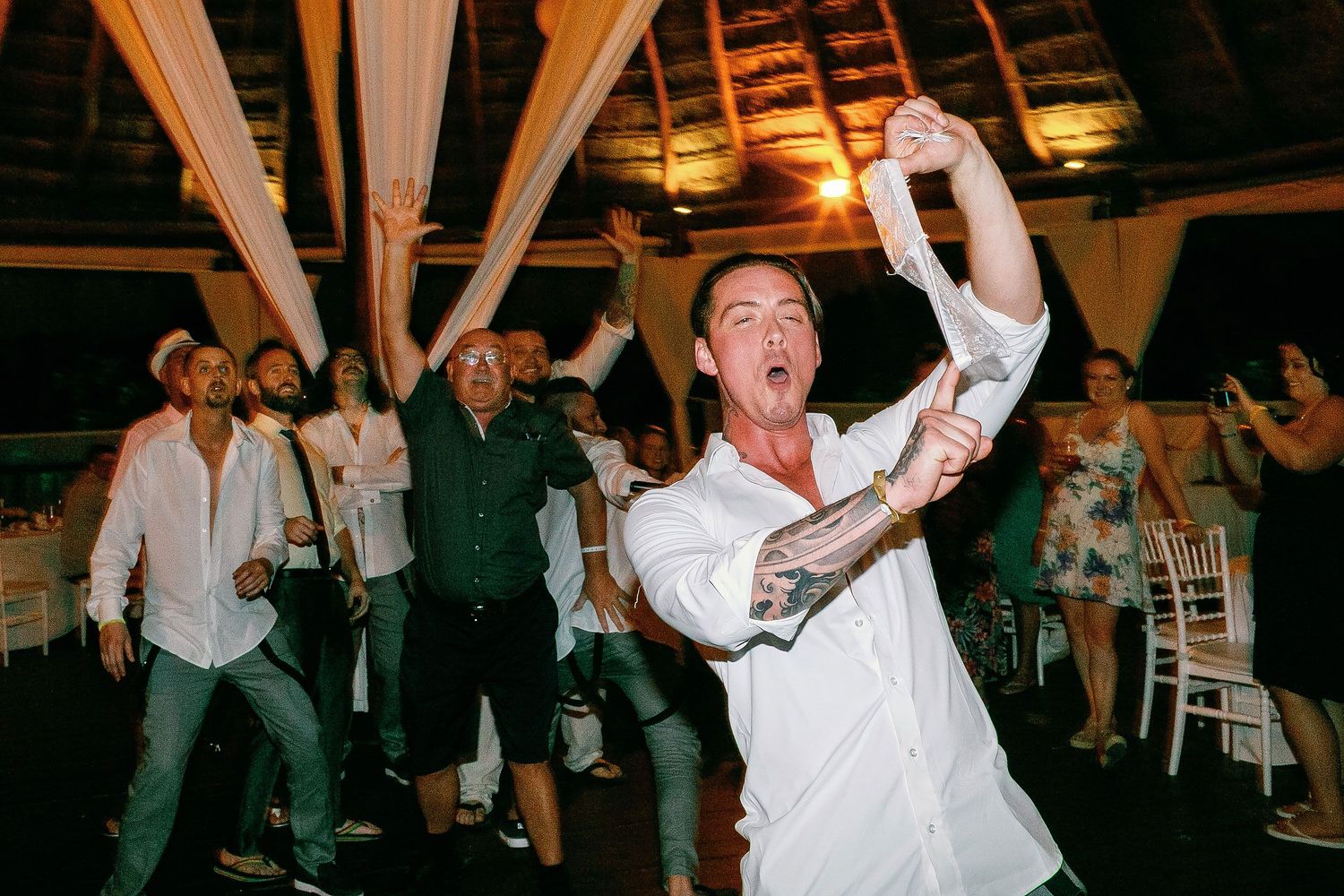 Scott holding up the garter as wedding guests cheer behind him