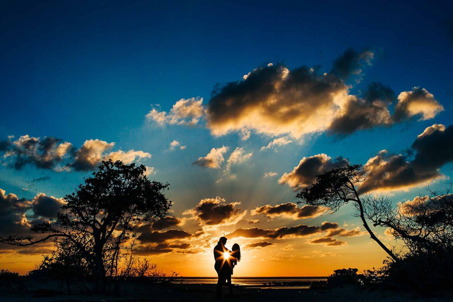 Romantic Cancun engagement photography silhouette at sunset with couple embracing beneath dramatic Riviera Maya skies