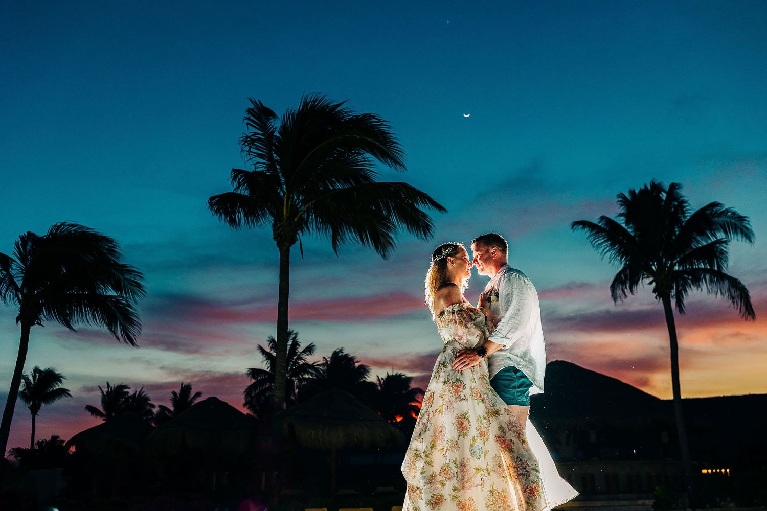 Dramatic sunset portrait of Autumn and Brian beneath palm trees and a crescent moon at Dreams Sapphire.