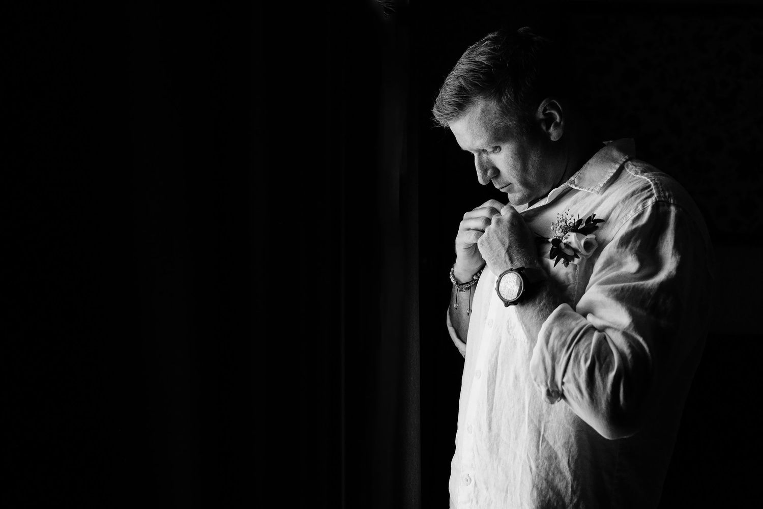 Brian fastening his white linen wedding shirt during groom preparation at Dreams Sapphire in Puerto Morelos.