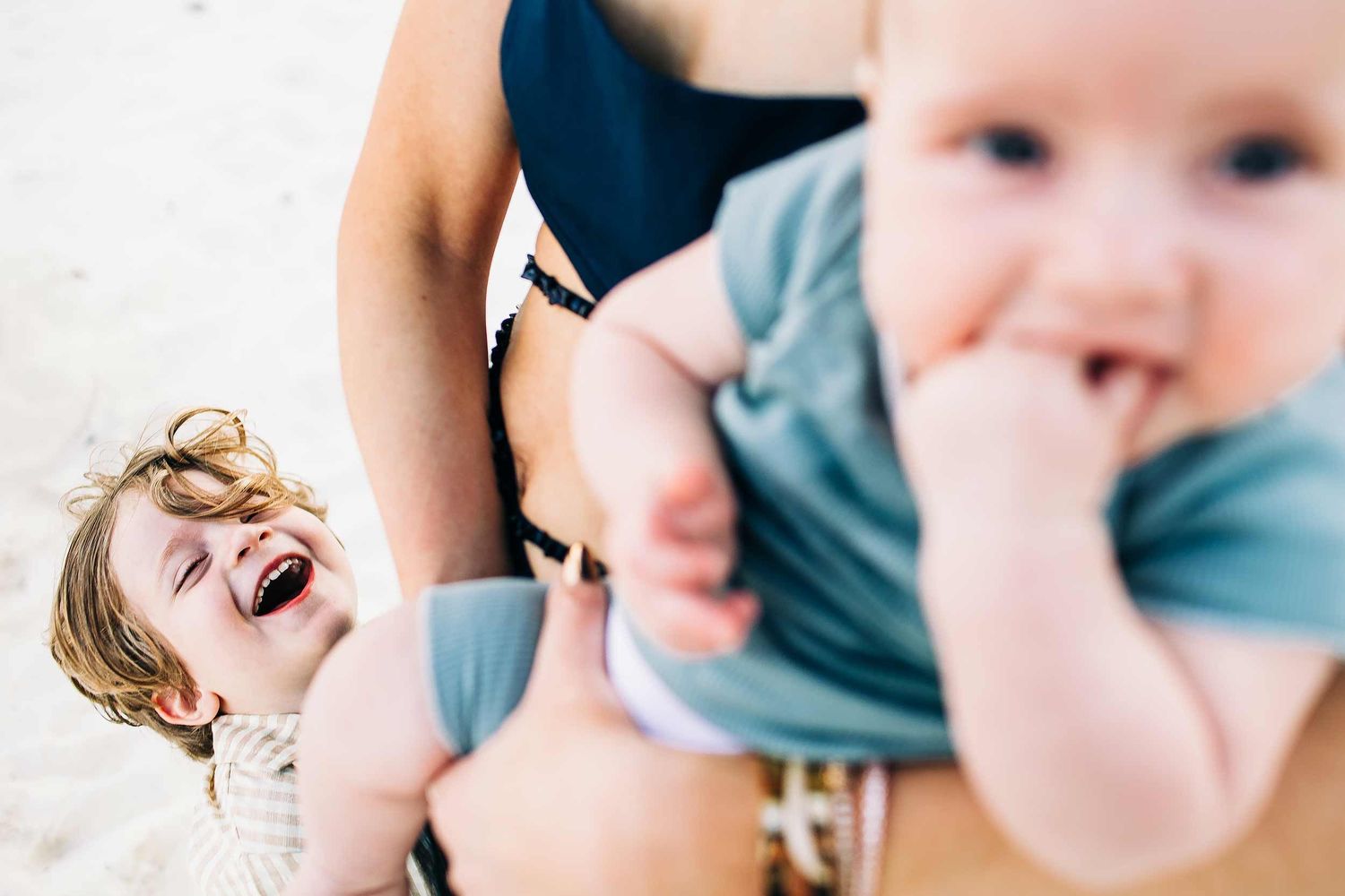 Smiling toddler laughing beside baby during a candid beach family session in Playa del Carmen.