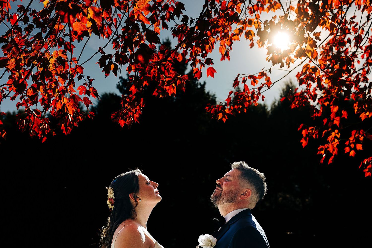 Samanta and Andrew facing each other in wedding attire beneath sunlit red autumn leaves in Michigan.