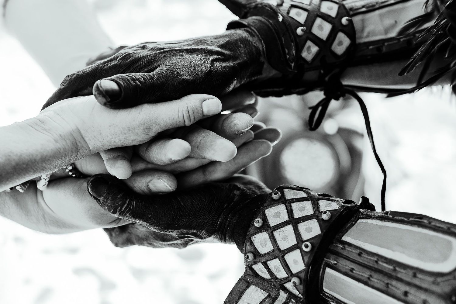 Sarah and Evish stack hands with ceremonial participants in a black-and-white close-up