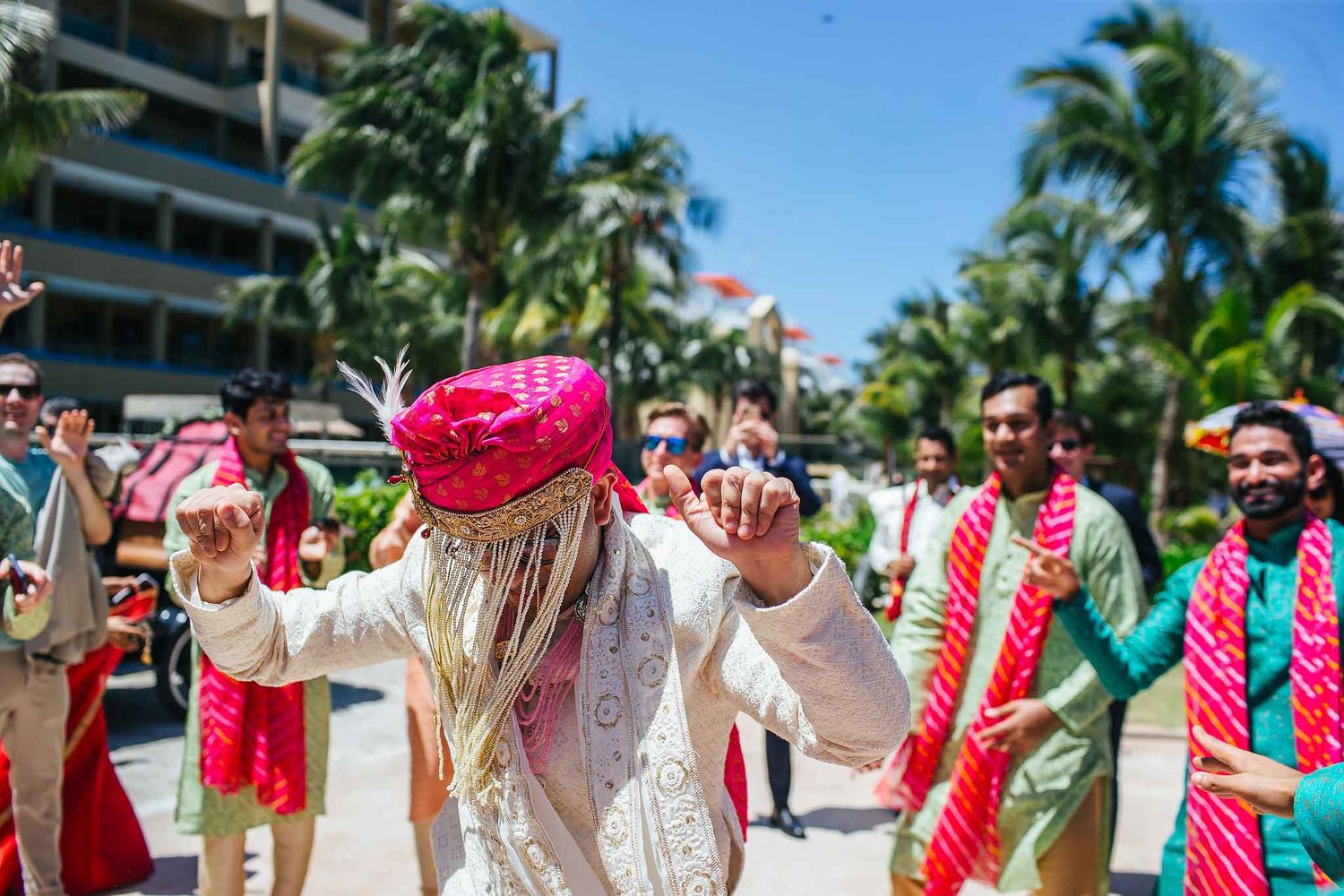 ndian groom dancing during vibrant baraat procession in Riviera Maya surrounded by guests in colorful traditional wedding attire.