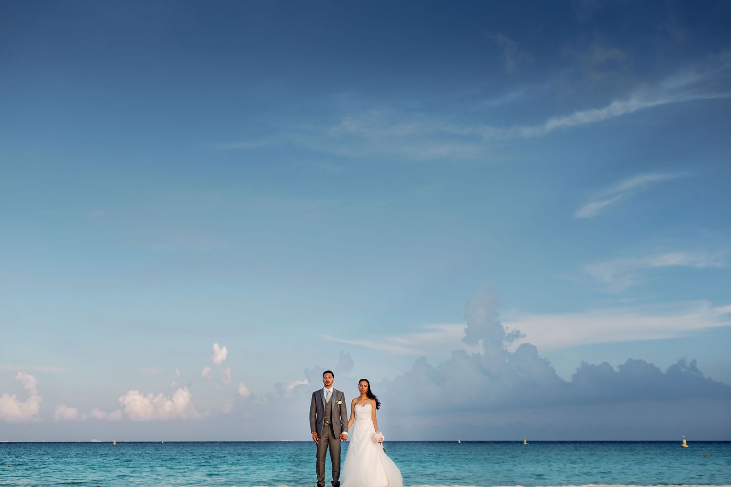 Felicitas and Keith stand hand in hand beneath an expansive sky in Playa del Carmen.