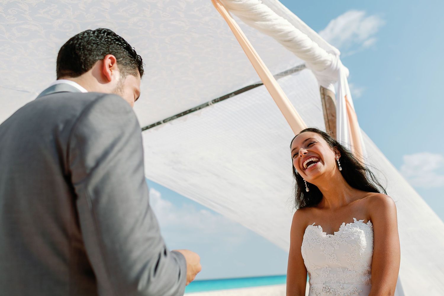 Felicitas laughs joyfully while standing with Keith during their beach ceremony.