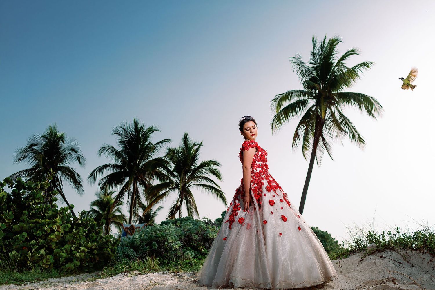 Quinceañera portrait in Playa del Carmen featuring an elegant floral gown, tropical palm trees, and Riviera Maya scenery.