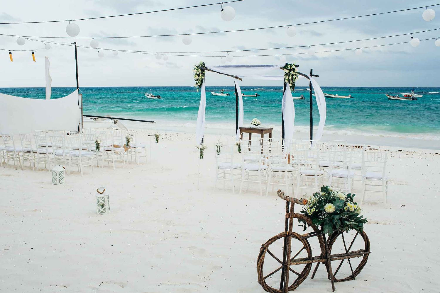 Tulum beach wedding ceremony setup with boho wooden arch, white chairs, and turquoise Caribbean ocean backdrop in Riviera Maya