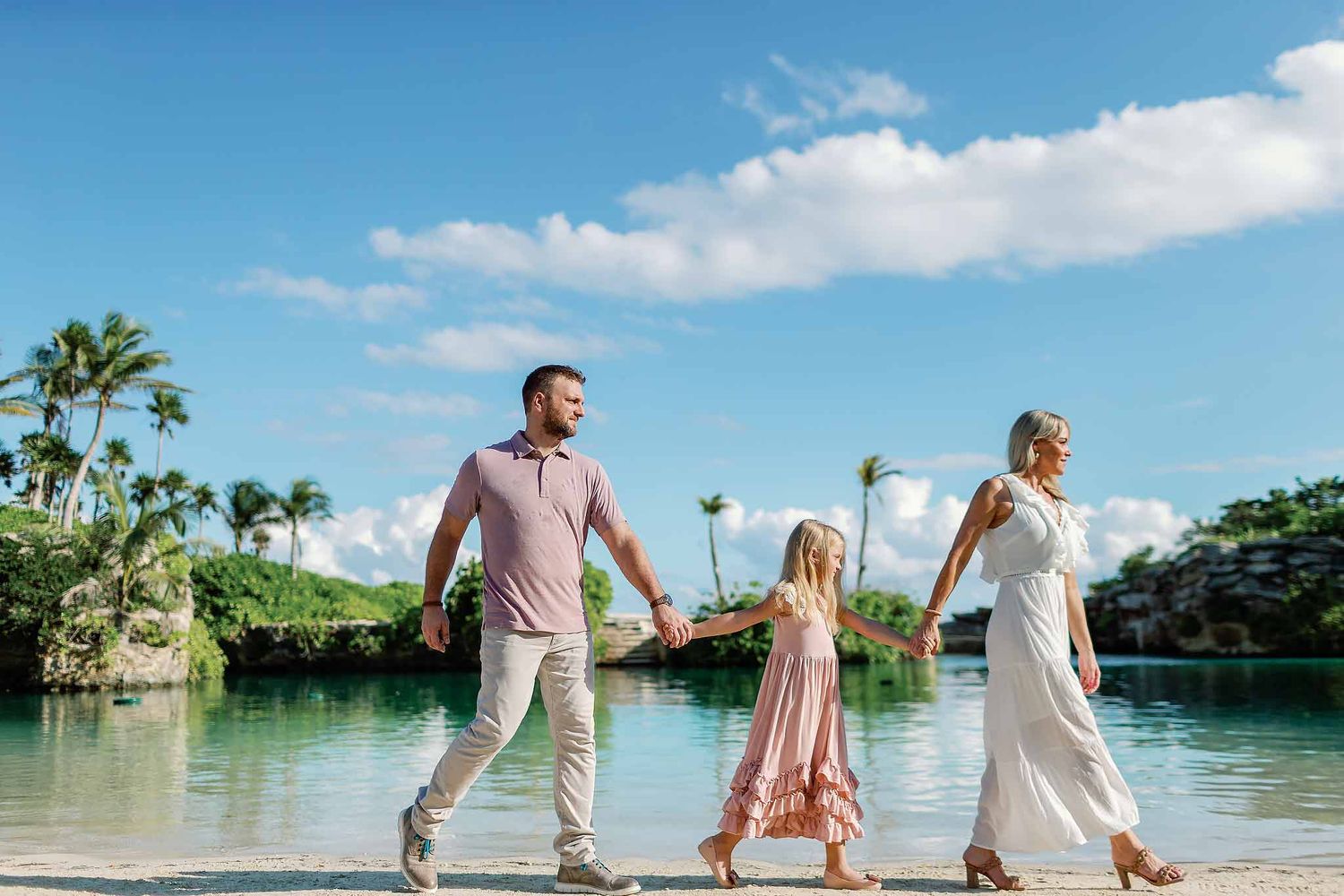 Family photoshoot in Cancun with parents and child walking together along the ocean beach with palm trees and blue sky
