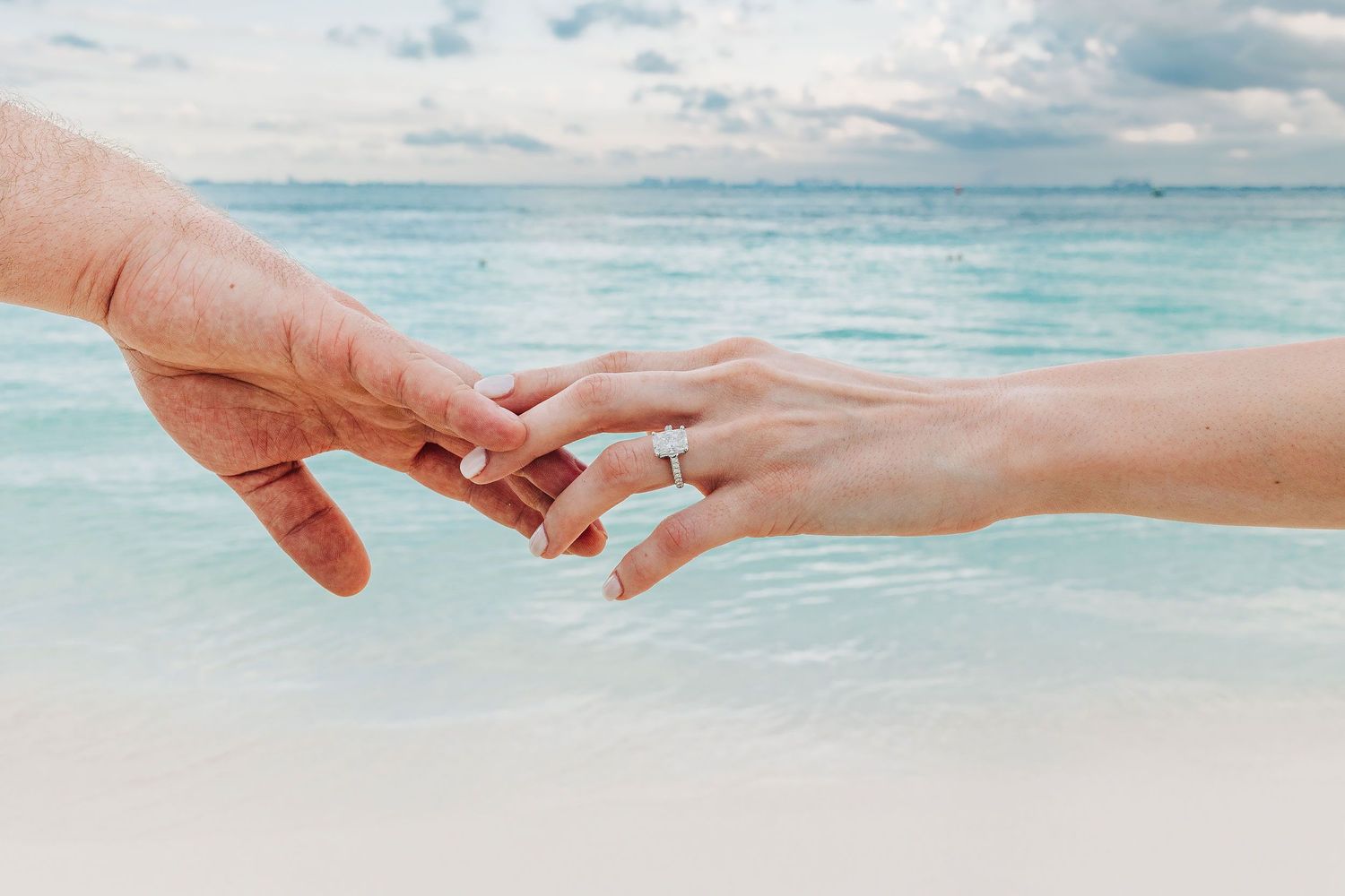 Close-up of Alexia’s engagement ring as she reaches for Sam’s hand beside the Caribbean.