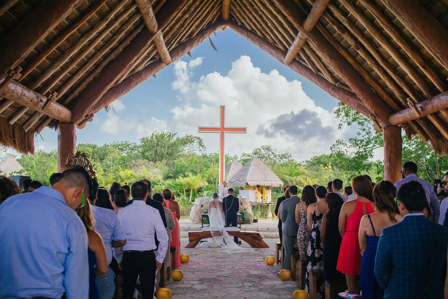 Catholic wedding ceremony at Xoximilco Riviera Maya chapel Capilla del Niño with bride and groom under cross and tropical open-air setting