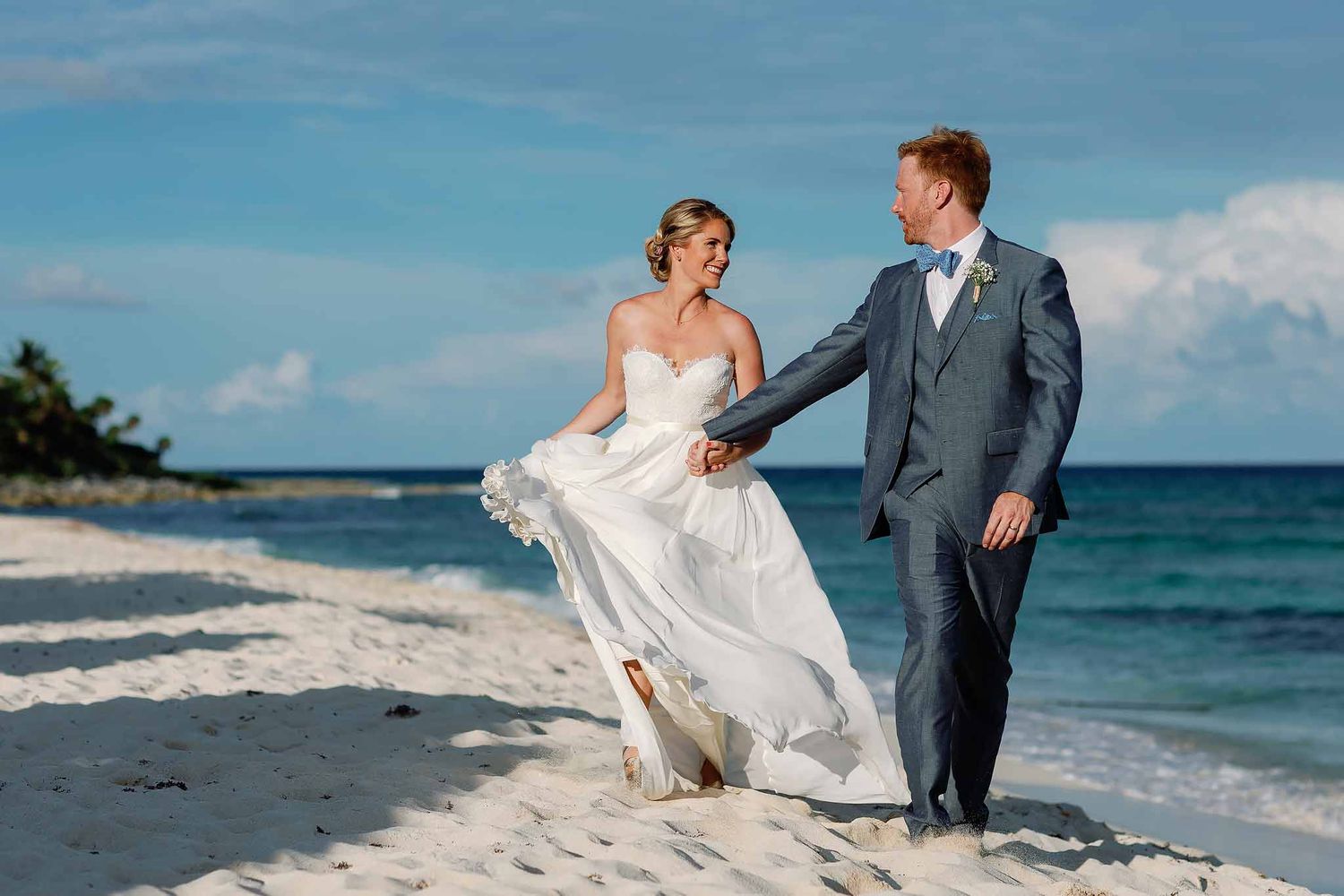Bride and groom walking on a Tulum beach holding hands with flowing wedding dress and Caribbean ocean backdrop in Riviera Maya