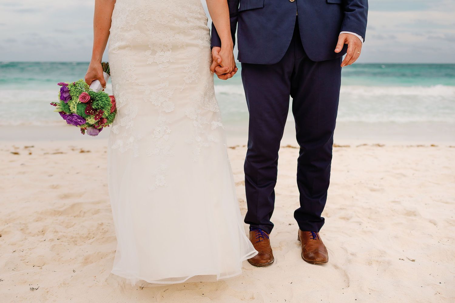 Close view of Ashley’s bouquet and the couple holding hands on the white sand in Tulum.