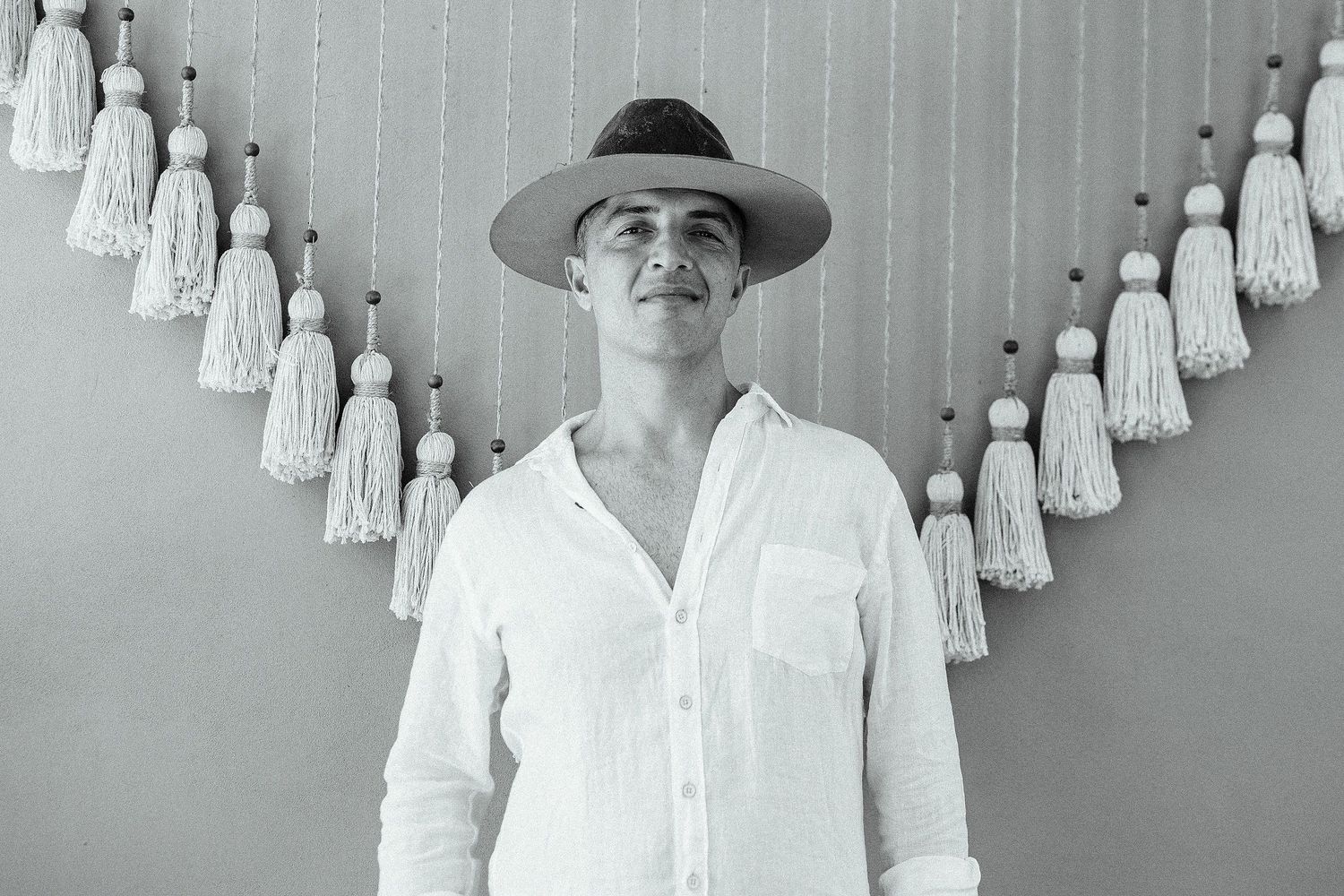 Black-and-white portrait of Evish in a wide-brim hat against hanging tassels.