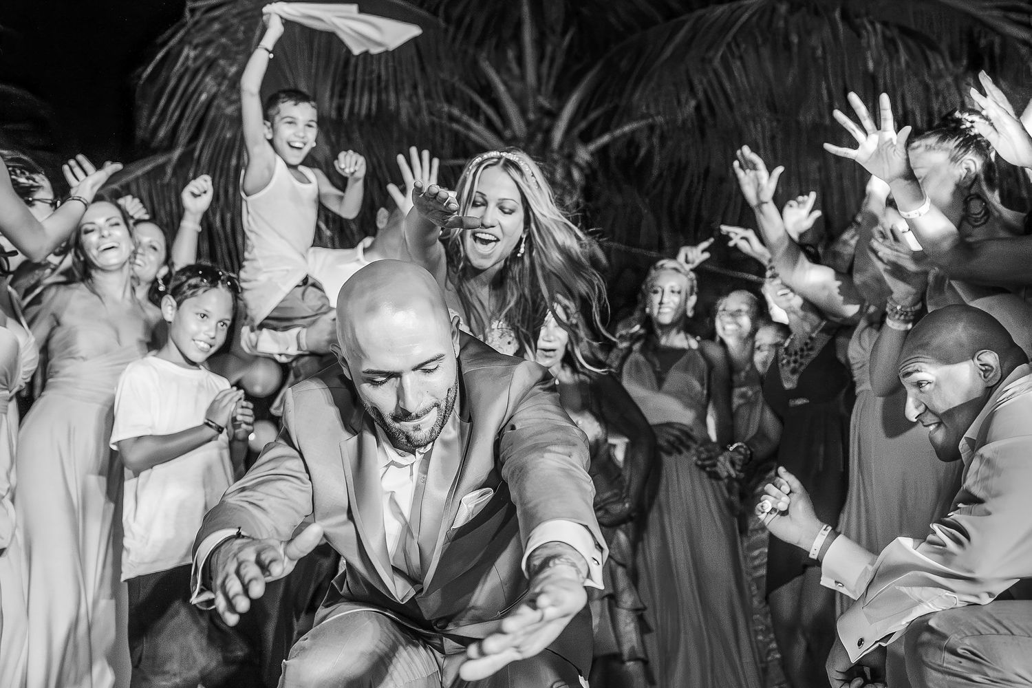 Black-and-white photograph of the bride and groom dancing as cheering guests surround them during their reception at Hard Rock Hotel Riviera