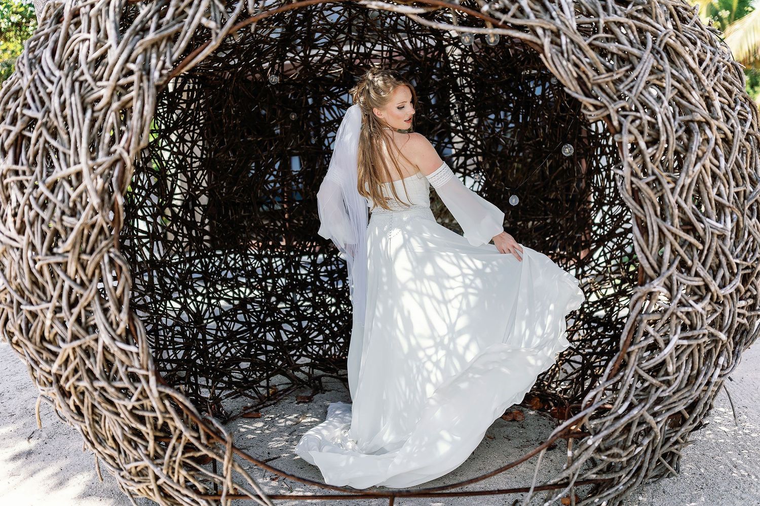 Nicole posing in her wedding dress inside a woven-wood structure during her Blue Venado wedding portraits in Playa del Carmen.