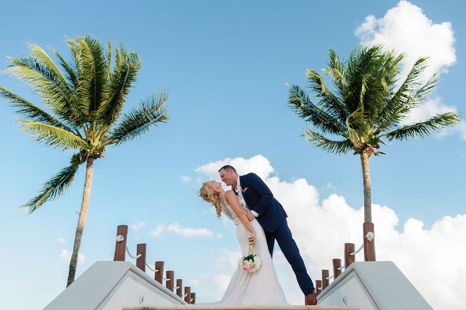Bride and groom sharing a playful romantic moment under palm trees during their wedding portrait session at Dreams Tulum in the Riviera Maya