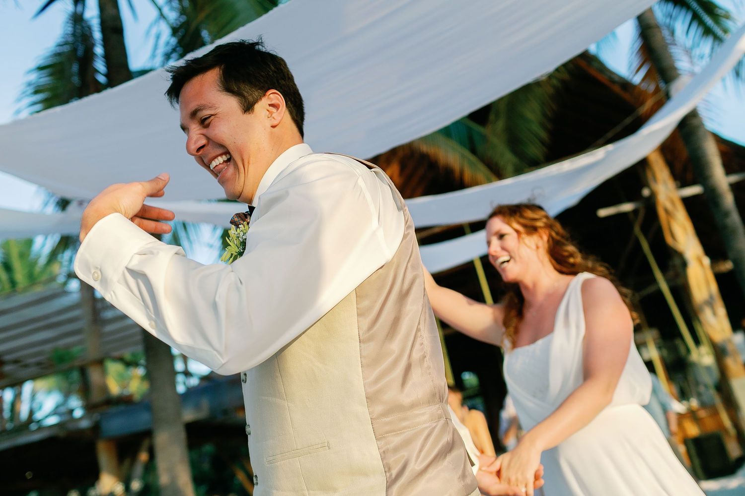 Carlos laughs on the dance floor while Li joins the Playa Norte beach reception behind him.