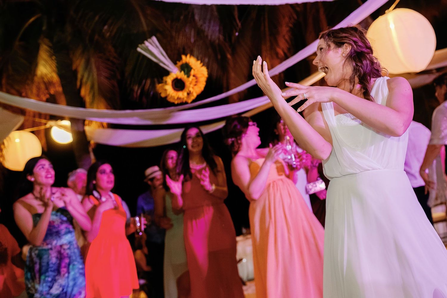 Li dances as friends cheer beneath pink lights and white draping at the beach reception.