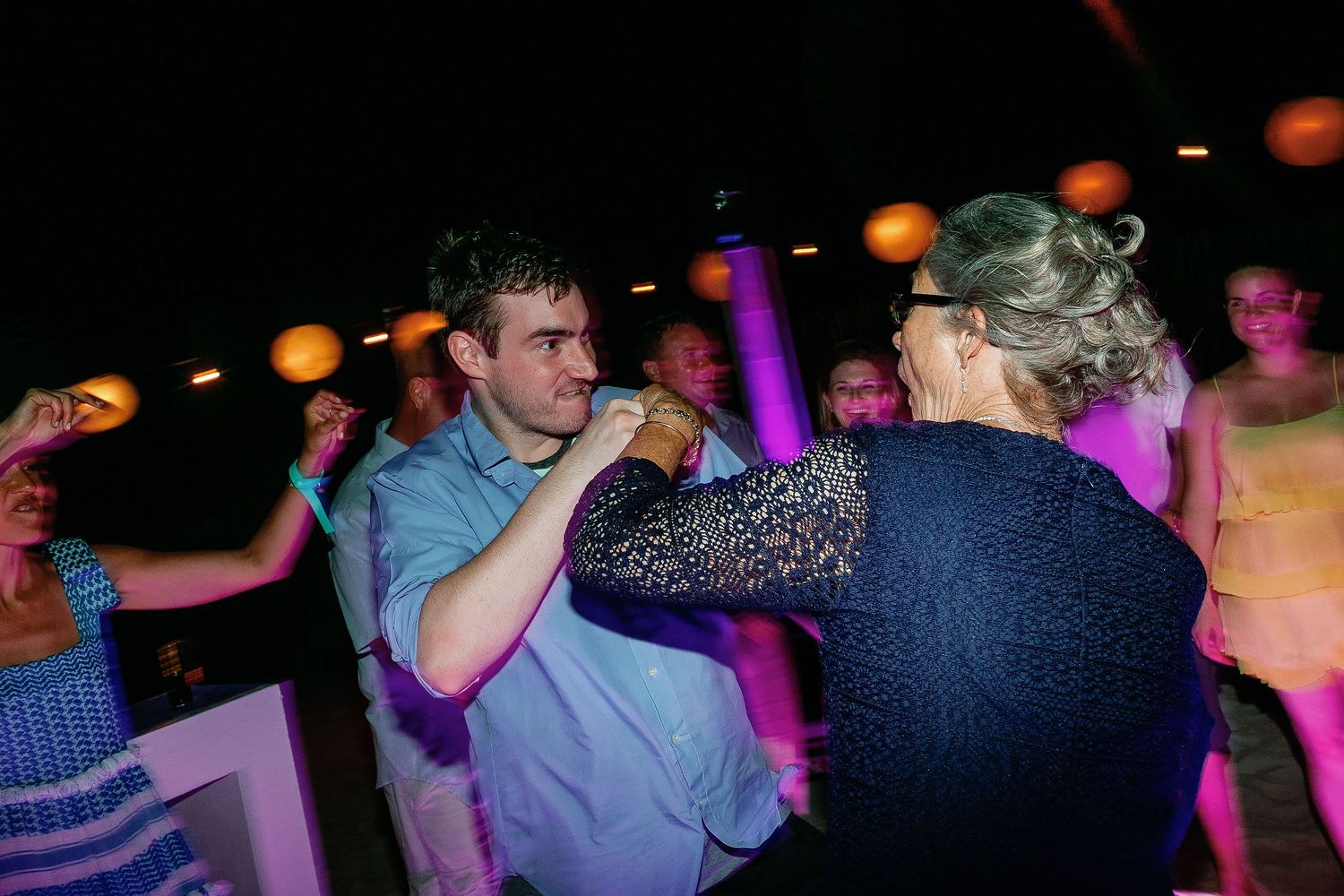 Two guests dance together beneath round lanterns and pink light at the outdoor Tulum reception.