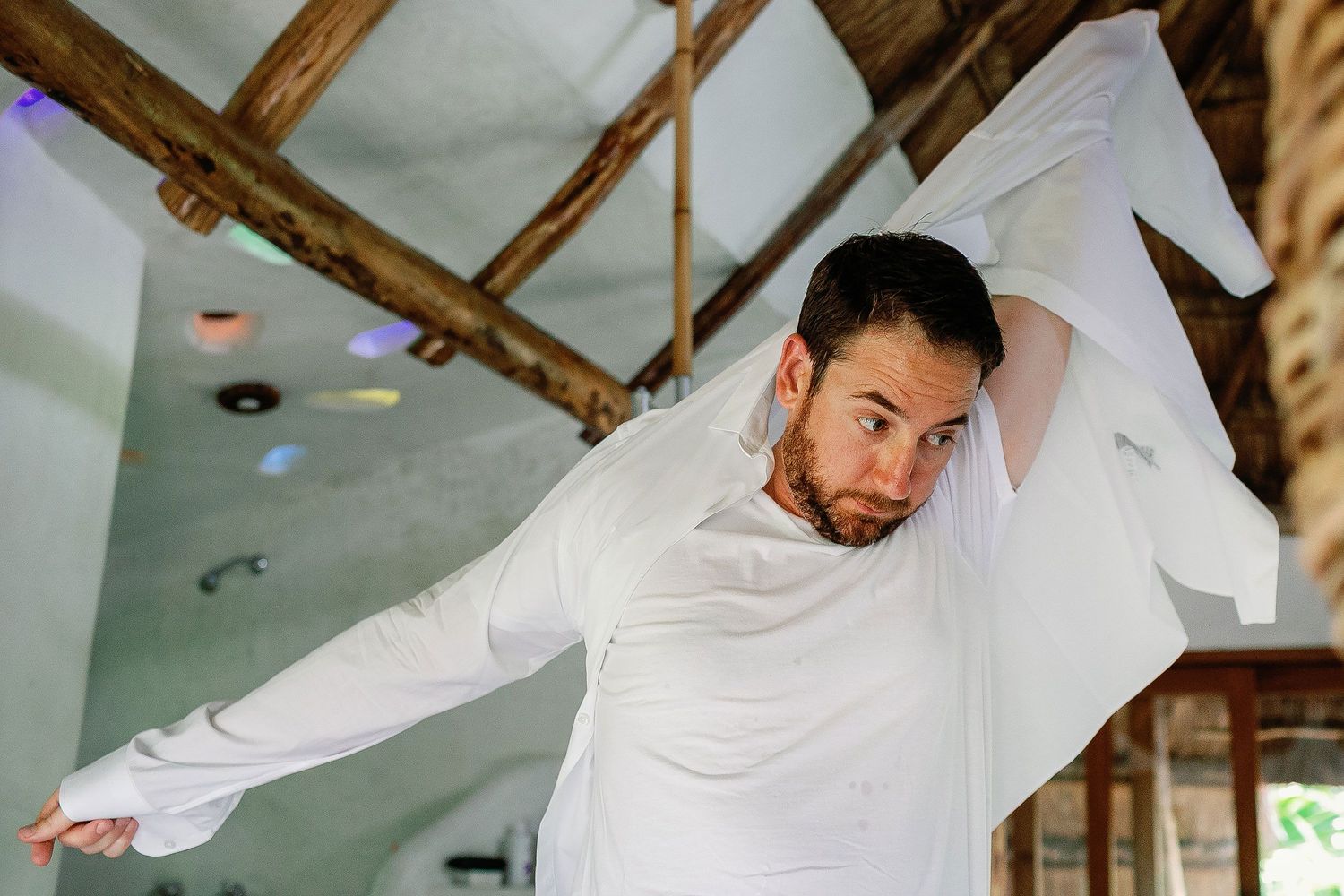 Matt puts on his white dress shirt while getting ready for his Tulum beach wedding.
