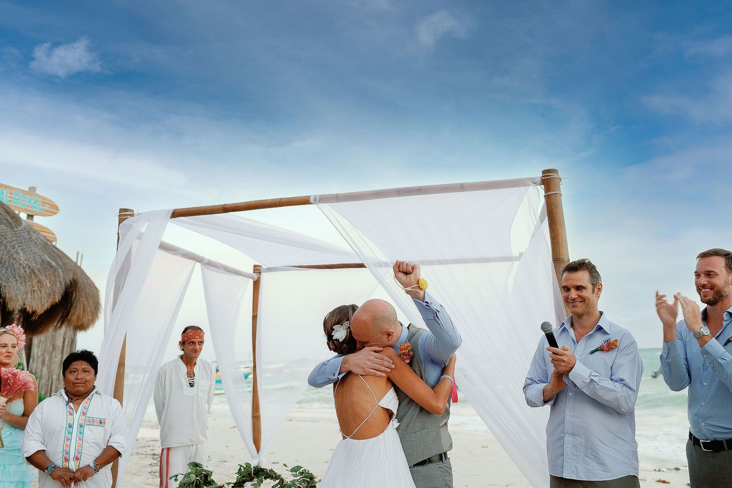 Juliana and Tom celebrate their marriage with a kiss beneath a white beach canopy.